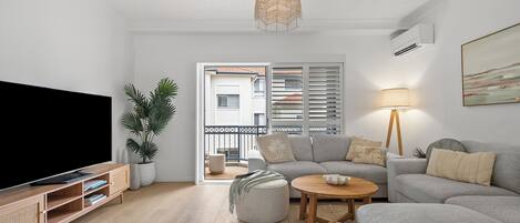 A living room with a TV, sofa, ottoman, coffee table, and a hanging light fixture.