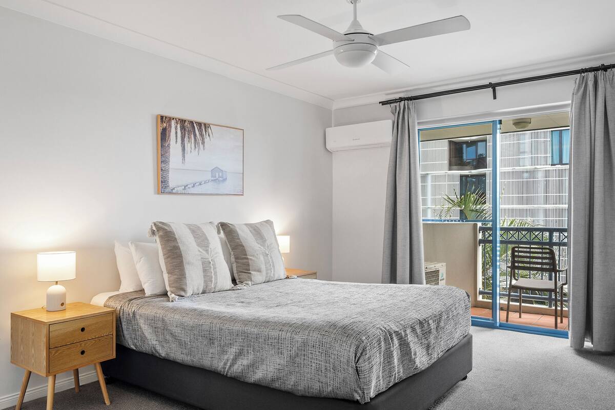 A bedroom with a bed, bedside table, lamp, and a painting on the wall.