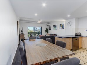 A modern kitchen with a dining area, featuring a wooden table, chairs, and a kitchen counter. - Bella Mare Beachside Apartments (Coolangatta)