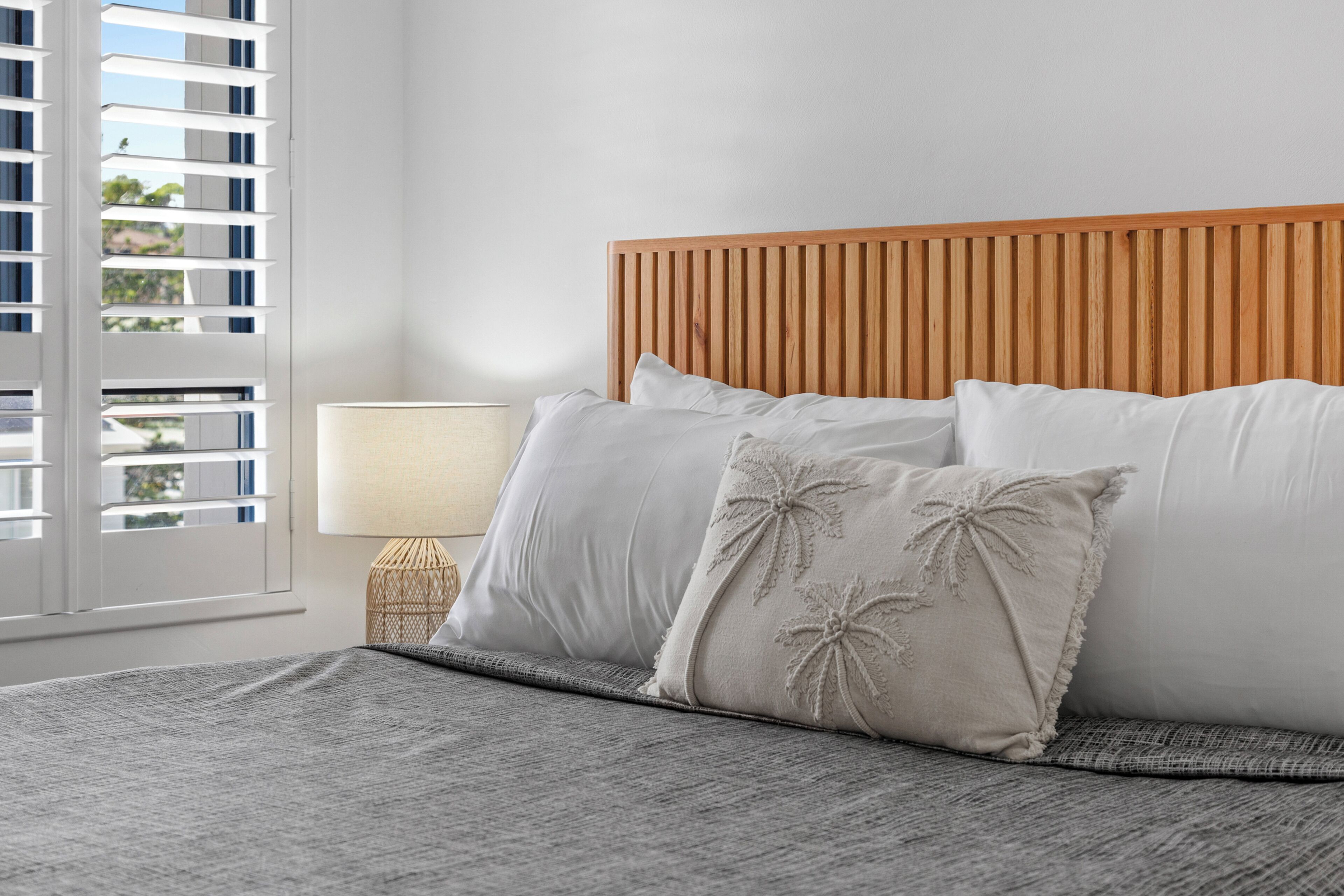 A bed with a wooden headboard, white pillows, a grey blanket, and a bedside lamp.