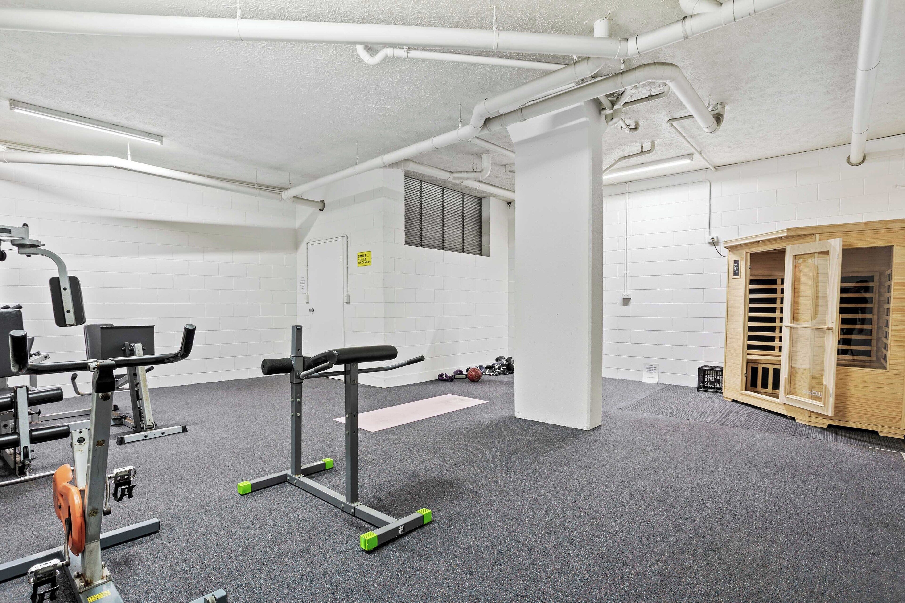 A gym with exercise equipment, a wooden cabinet, and a white wall with a window.