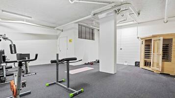 A gym with exercise equipment, a wooden cabinet, and a white wall with a window.