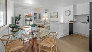 Une cuisine moderne avec des meubles blancs, une table à manger au plateau en verre et des chaises en osier.