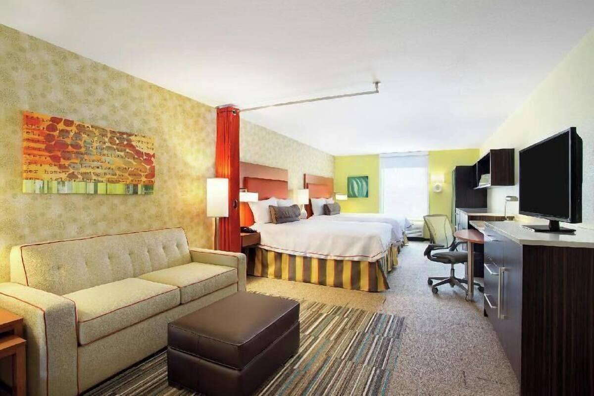 Ein Hotelzimmer mit einem Bett, einem Sofa, einem Schreibtisch, einem Fernseher und einem Bild an der Wand.