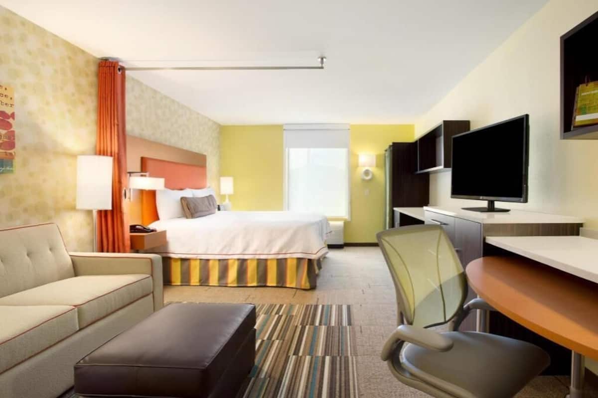 Ein Hotelzimmer mit Bett, Sofa, Schreibtisch, Stuhl, Fernseher und Fenster.
