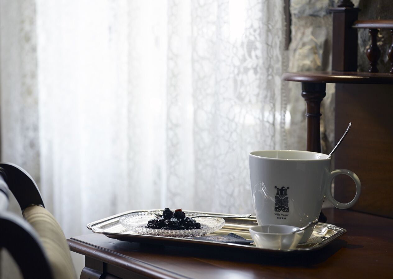 Una taza blanca con una cuchara sobre una bandeja, colocada en una mesa de madera cerca de una silla.