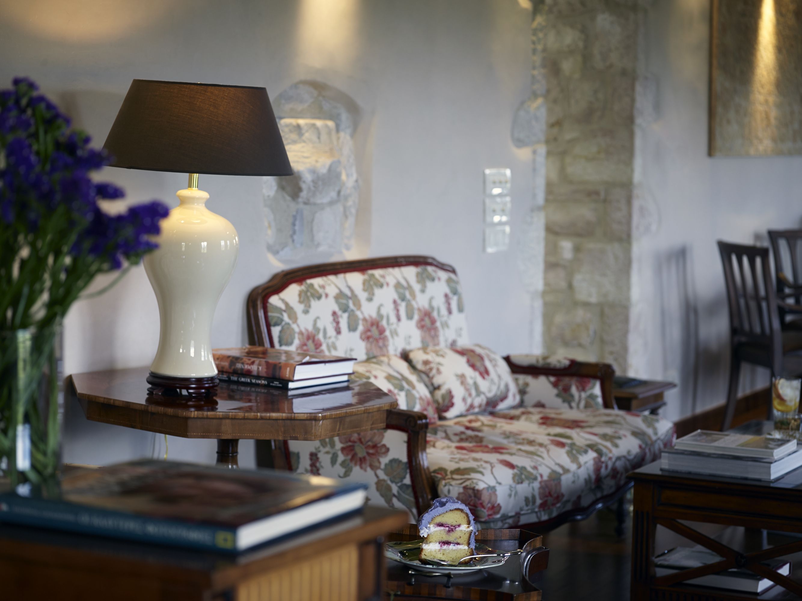 A cozy living room with a floral sofa, a side table with a lamp, and a vase with flowers.