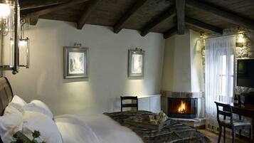 A cozy bedroom with a fireplace, a bed with white linens, and two framed pictures on the wall.