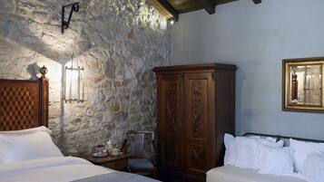 A bedroom with stone walls, wooden furniture, and a bed with white linens.