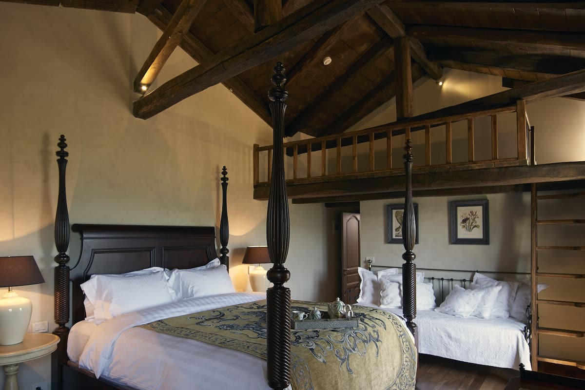 A four-poster bed with a canopy, a bedside table with a lamp, and a wooden ladder to the right.
