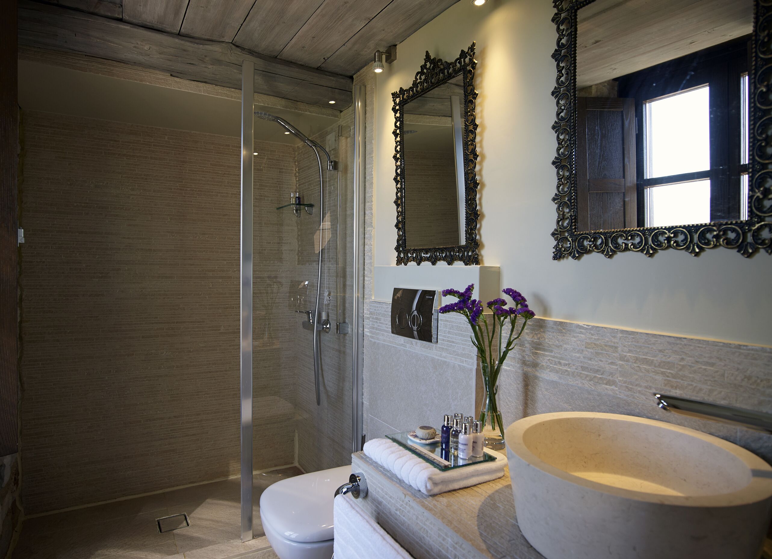 Un baño moderno con ducha de vidrio, un espejo grande y un lavamanos redondo.