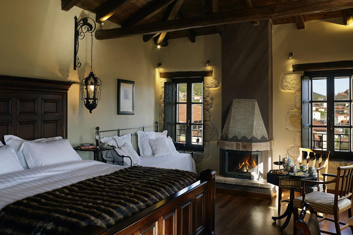 A bedroom with a large bed, a fireplace, and a view of the outside.