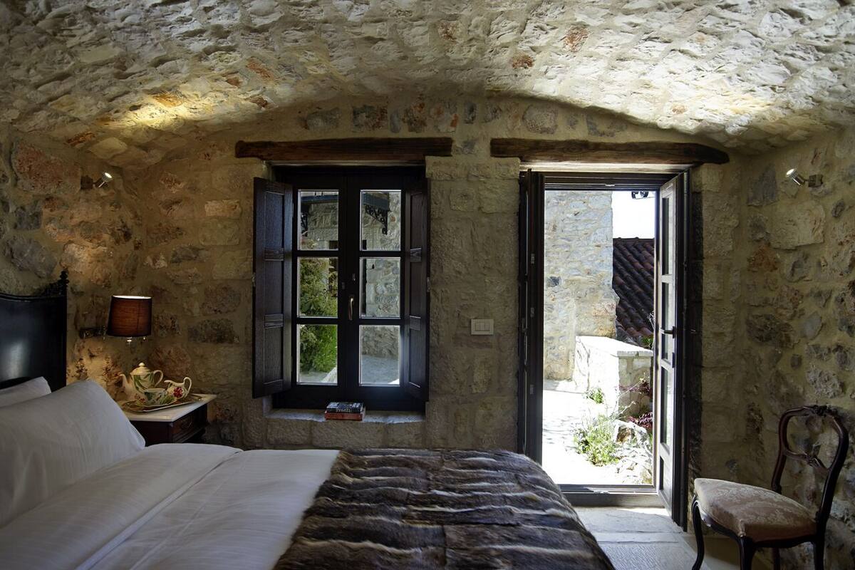 A stone-walled bedroom with a bed, a window, and a chair.