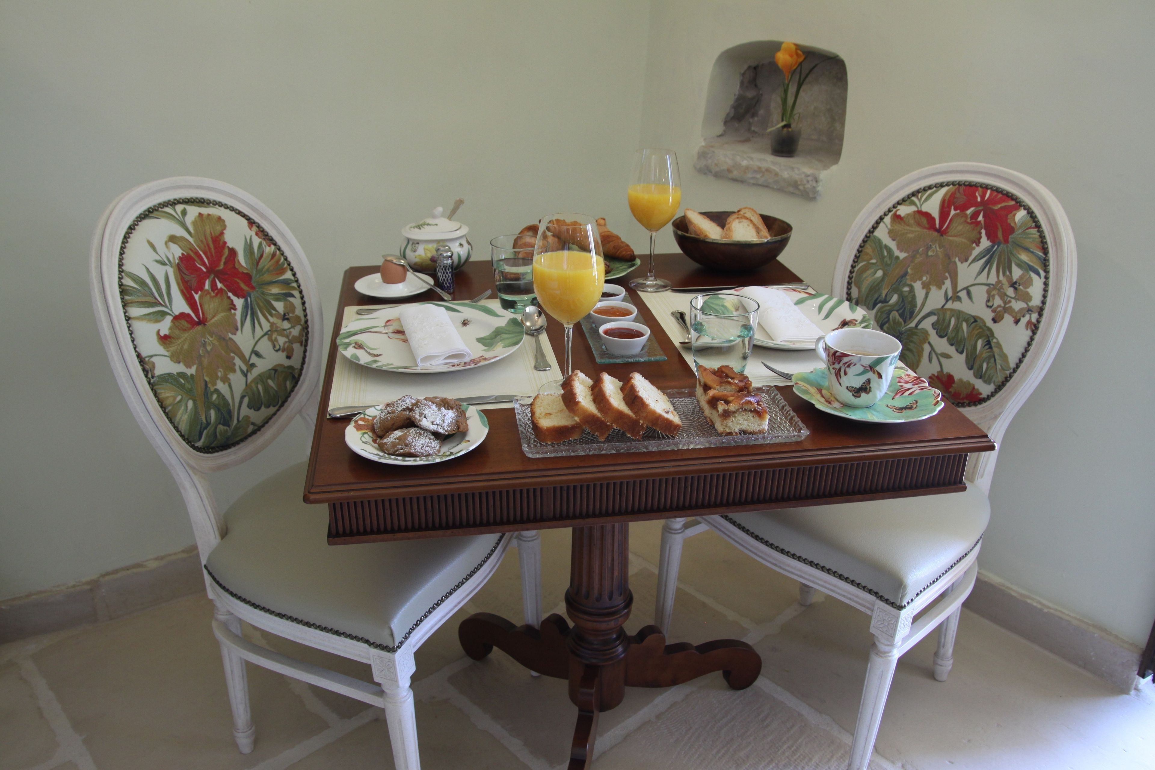 Mesa de jantar posta com itens de café da manhã, incluindo pães, bolos e copos de suco.