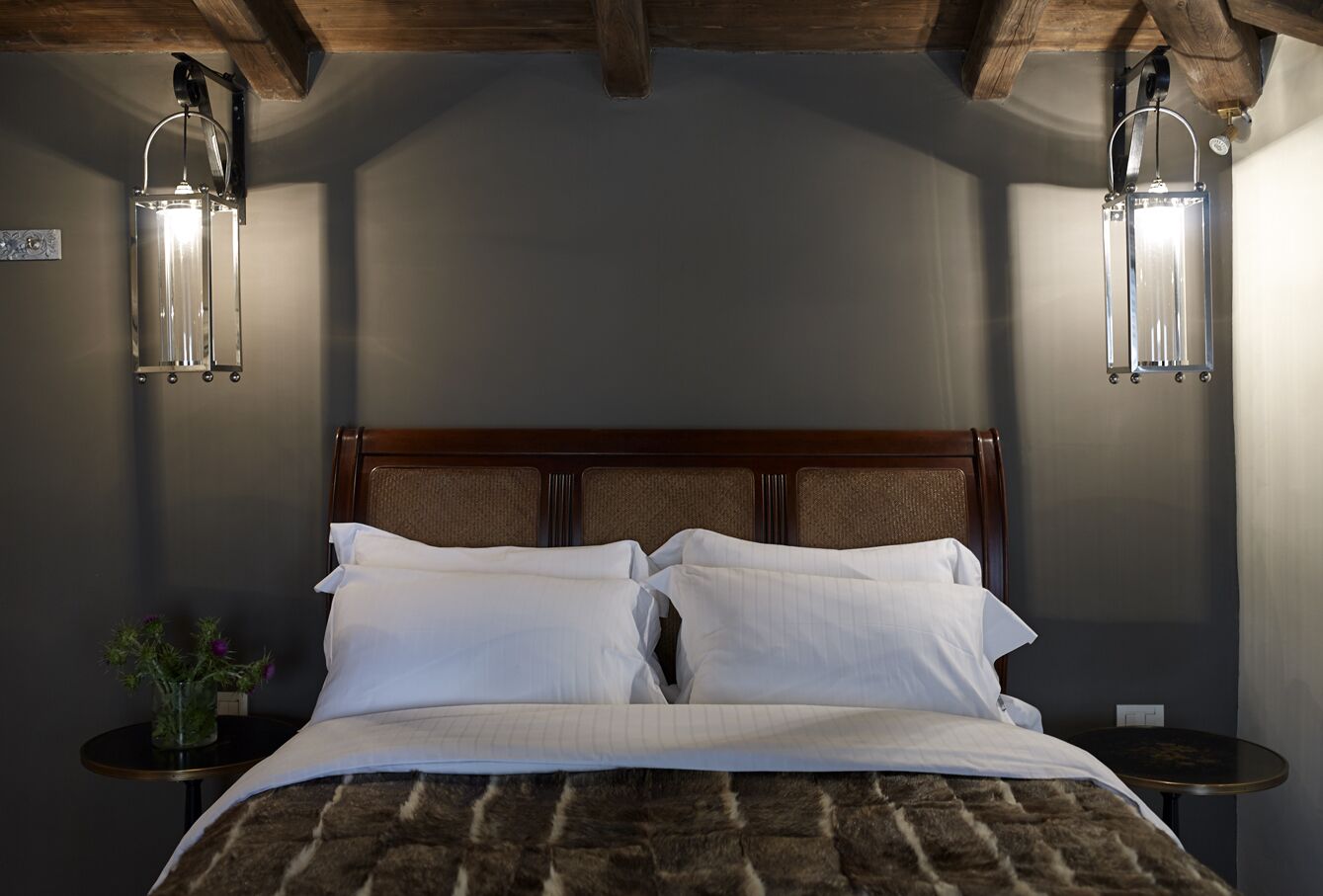 A neatly made bed with white linens, two bedside tables with lamps, and a wooden headboard.
