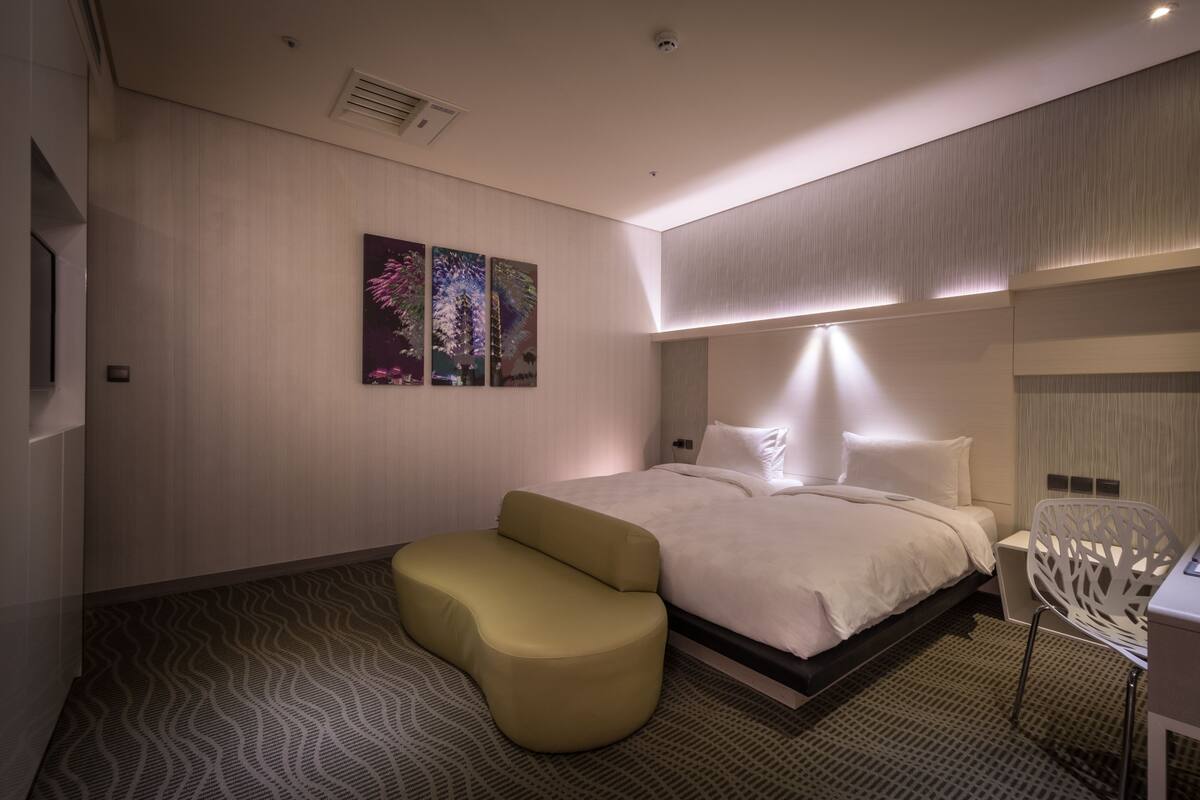 Quarto de hotel moderno com cama, área de estar e obras de arte na parede.