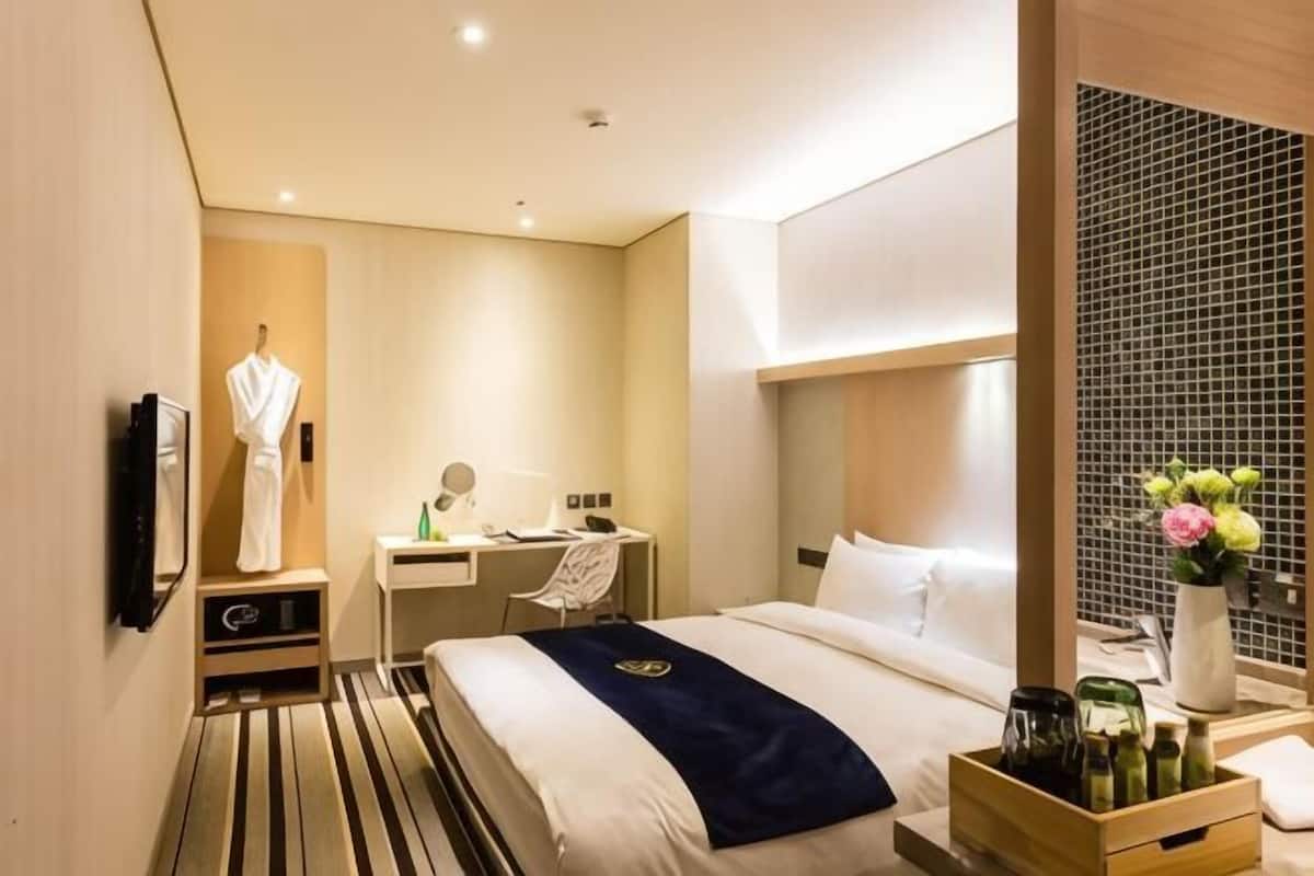 Quarto de hotel com cama, escrivaninha, cadeira e um pequeno armário.