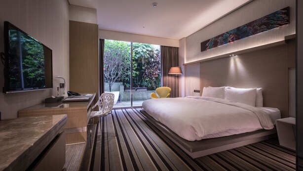 A modern hotel room with a large bed, a desk, and a chair. There is a balcony with a view of trees. - Taipei 101 SPARKLE Hotel (Taipei)