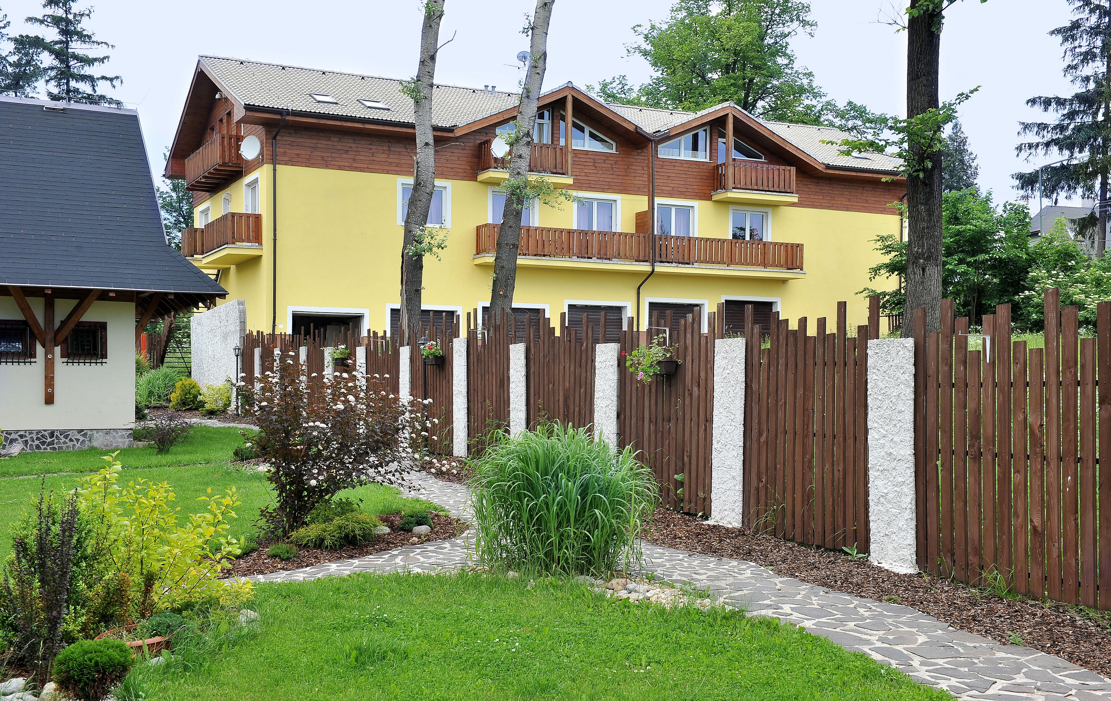 Un edificio giallo di due piani con un balcone in legno, circondato da una recinzione in legno e un vialetto in pietra.