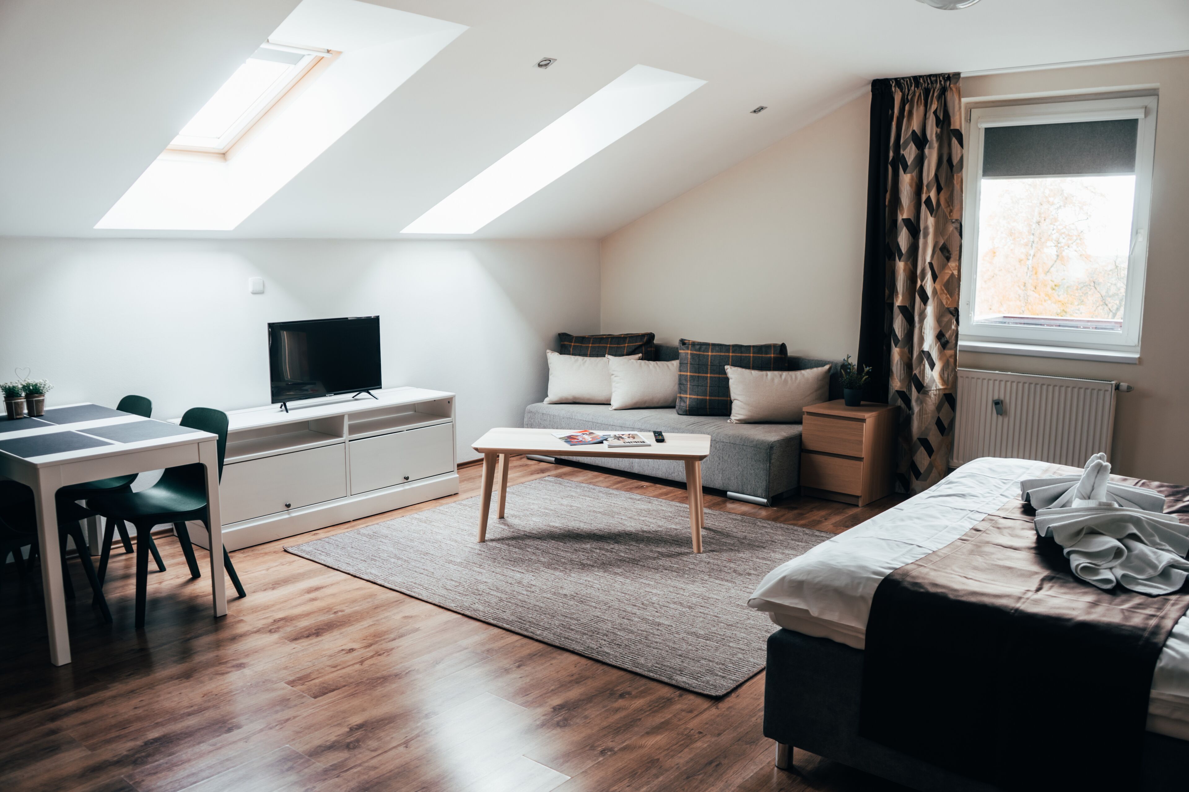 A modern, well-lit room with a loft bed, a desk, a television, and a window with curtains.