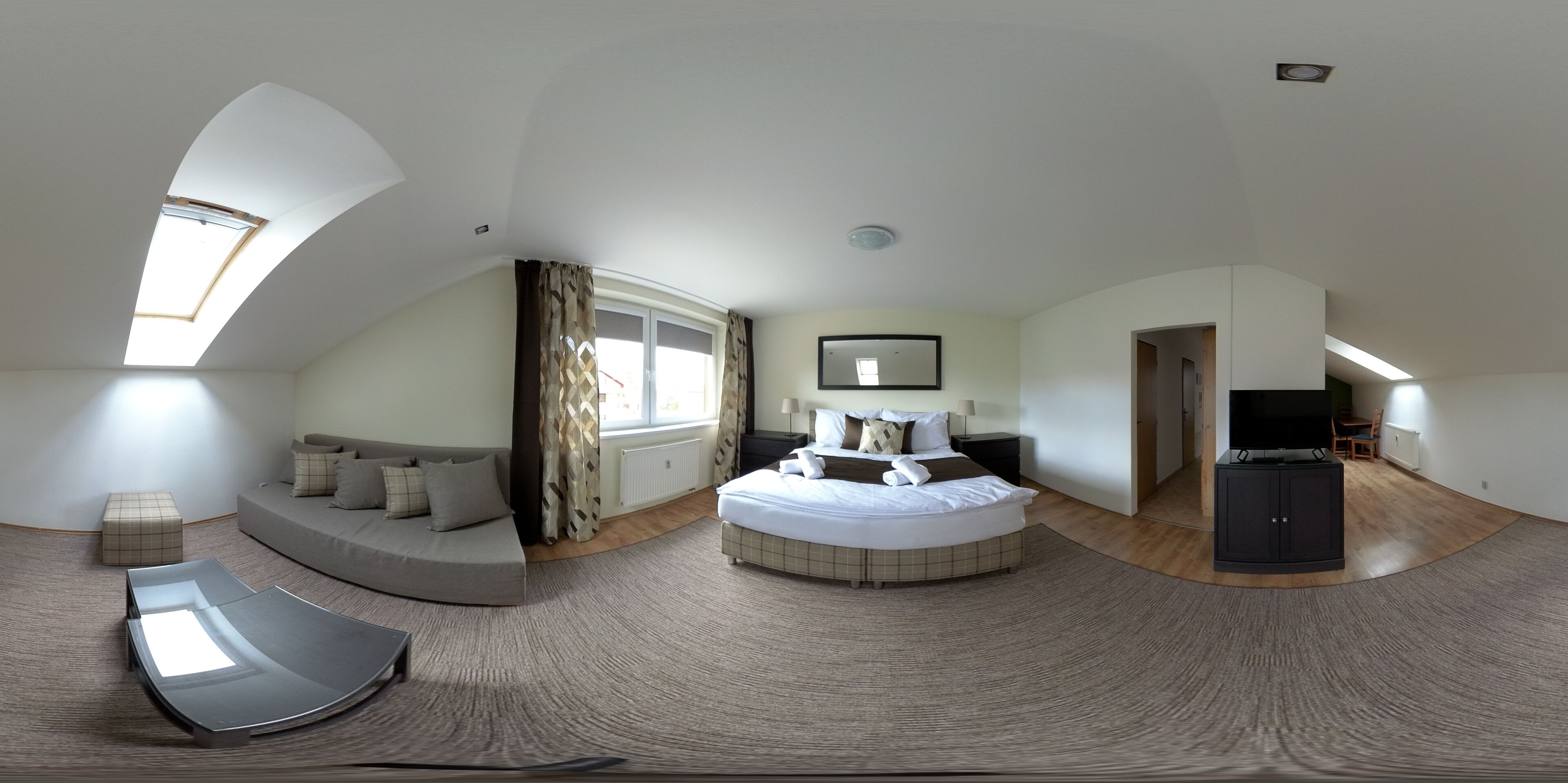 A panoramic view of a modern bedroom with a skylight, a curved sofa, a round bed, and a television.