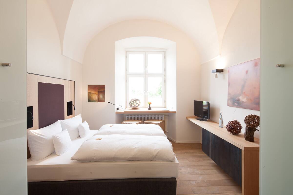 Una habitación de hotel con dos camas, un escritorio, un ventanal y obras de arte en las paredes.