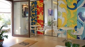 A hotel lobby with a colorful mural, white chairs, a small table, and a reception area. - Porta del Tocco Design Rooms (Taormina)