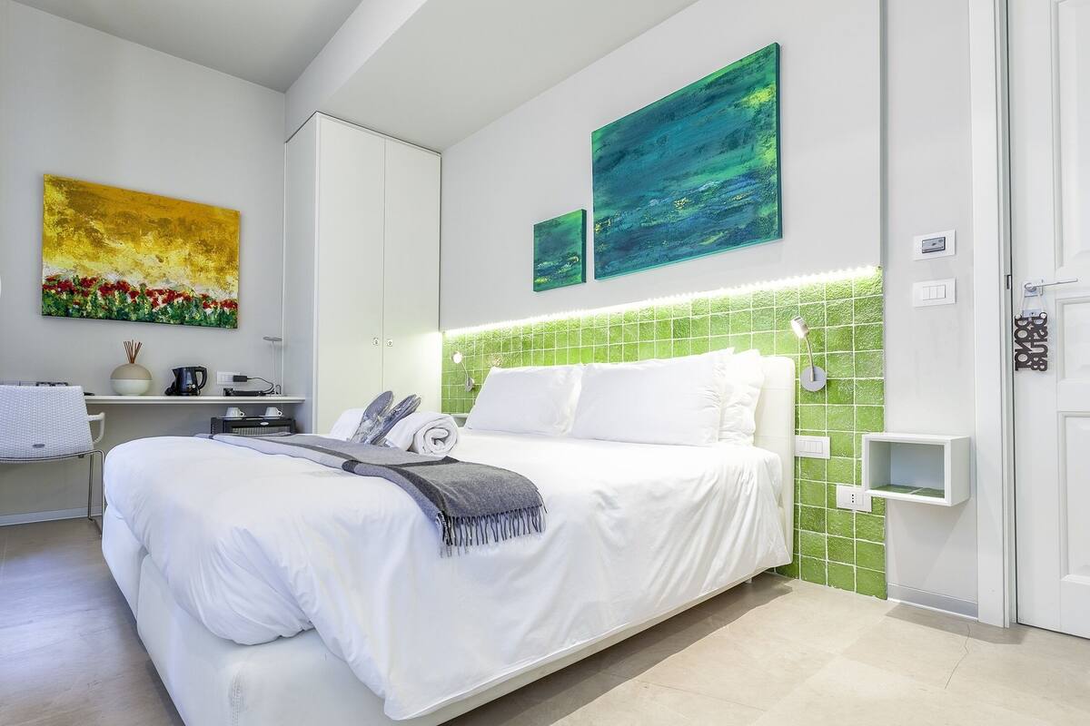 A modern bedroom with a bed, a nightstand, a lamp, and artwork on the walls.