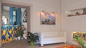 A modern living room with a white sofa, a colorful abstract painting, a large mirror, and a potted plant. - Porta del Tocco Design Rooms (Taormina)