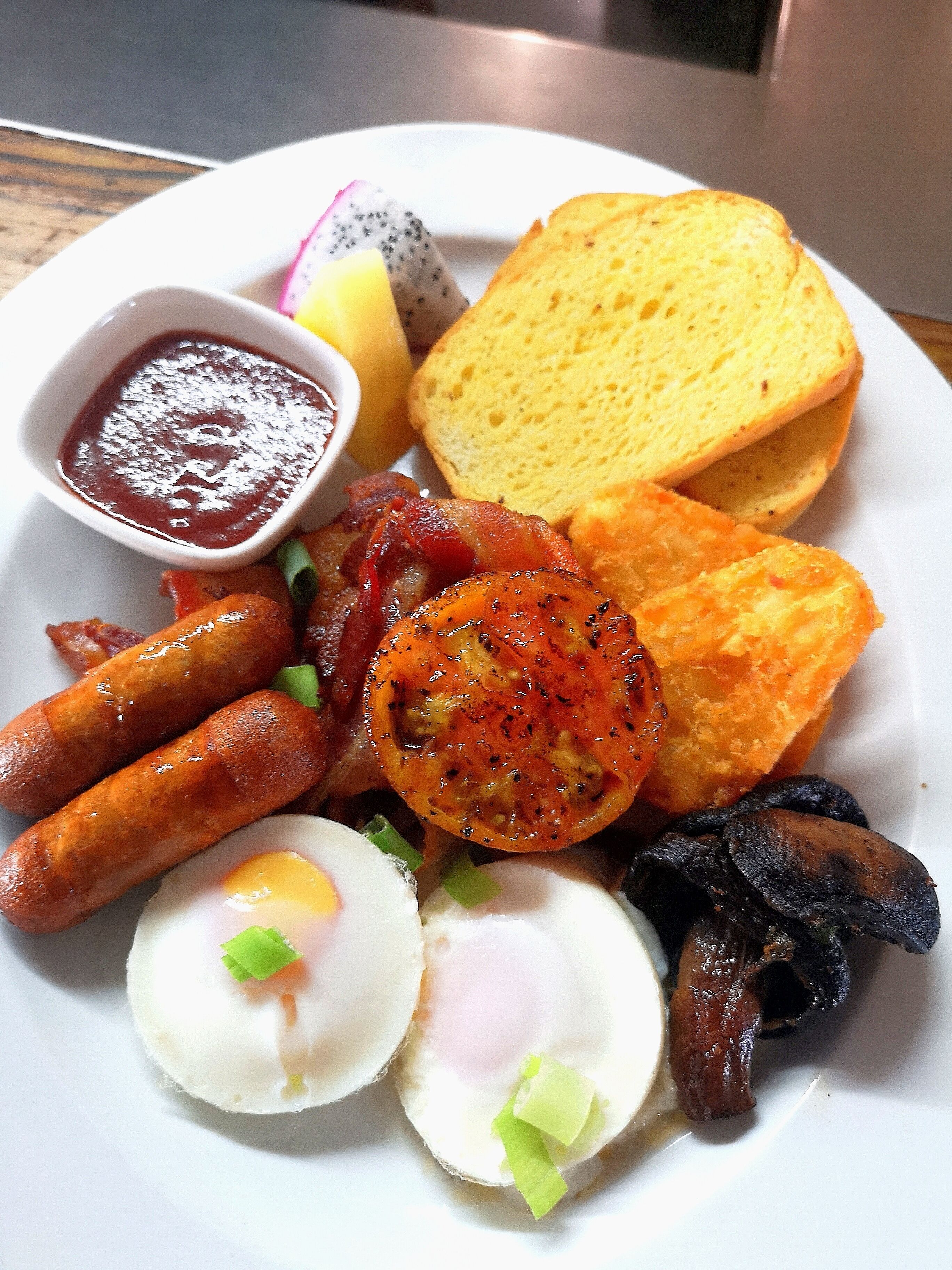 A plate of breakfast food including sausages, eggs, toast, and a side of sauce.