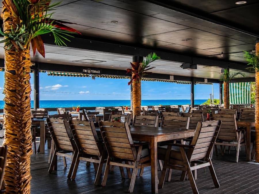 Un espace de restauration en plein air avec des tables et des chaises en bois, entouré de palmiers et offrant une vue sur la plage.
