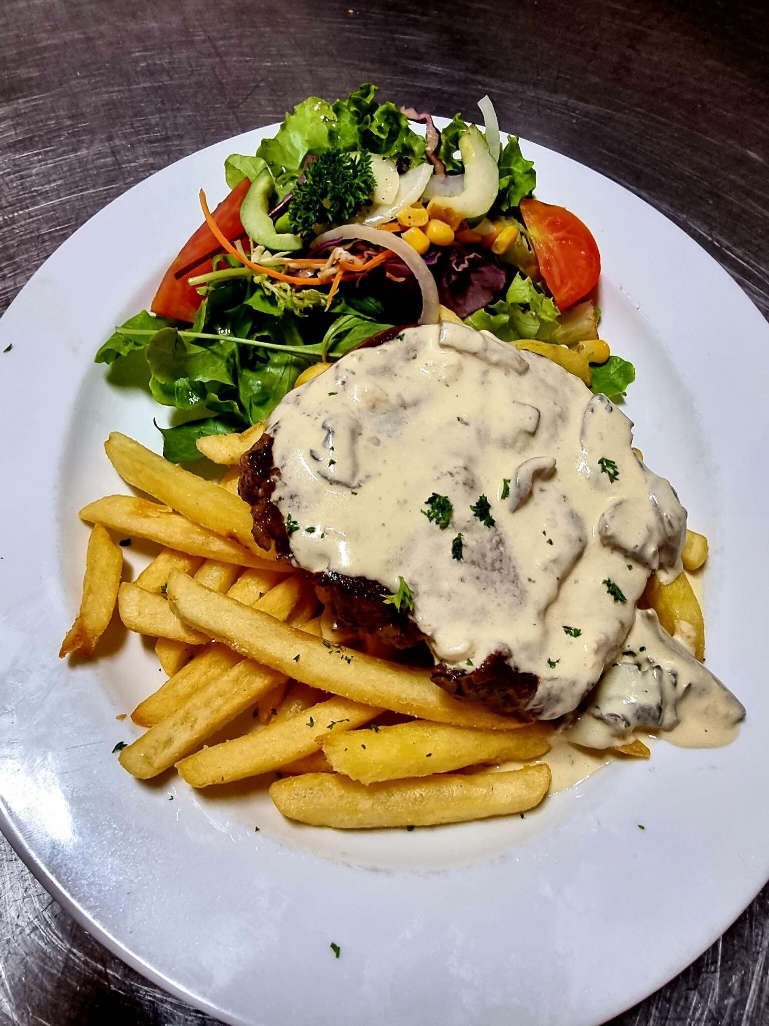 A plate with a meat patty topped with creamy sauce, accompanied by French fries and a side salad.