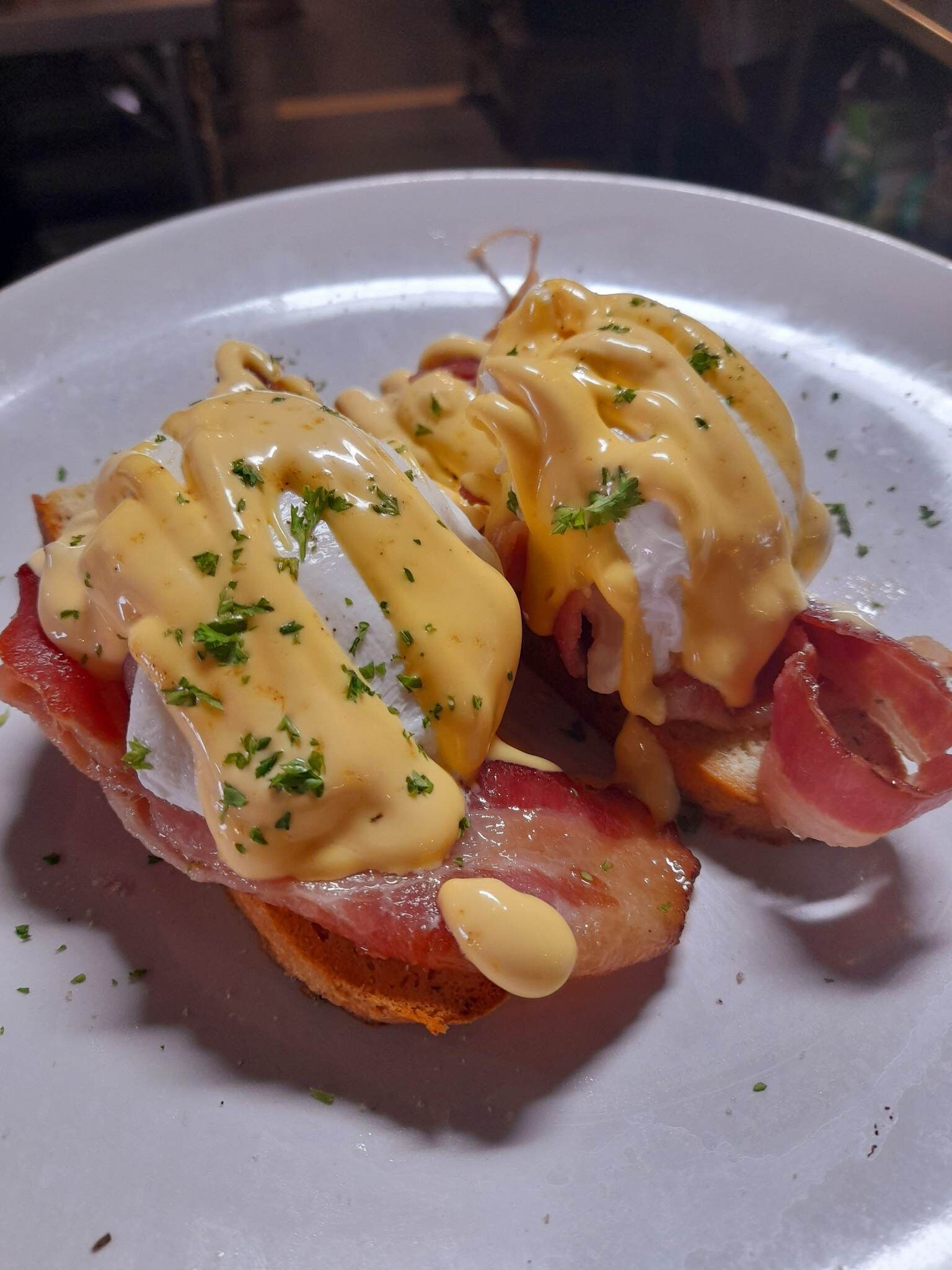 A plate of eggs benedict with ham and hollandaise sauce.