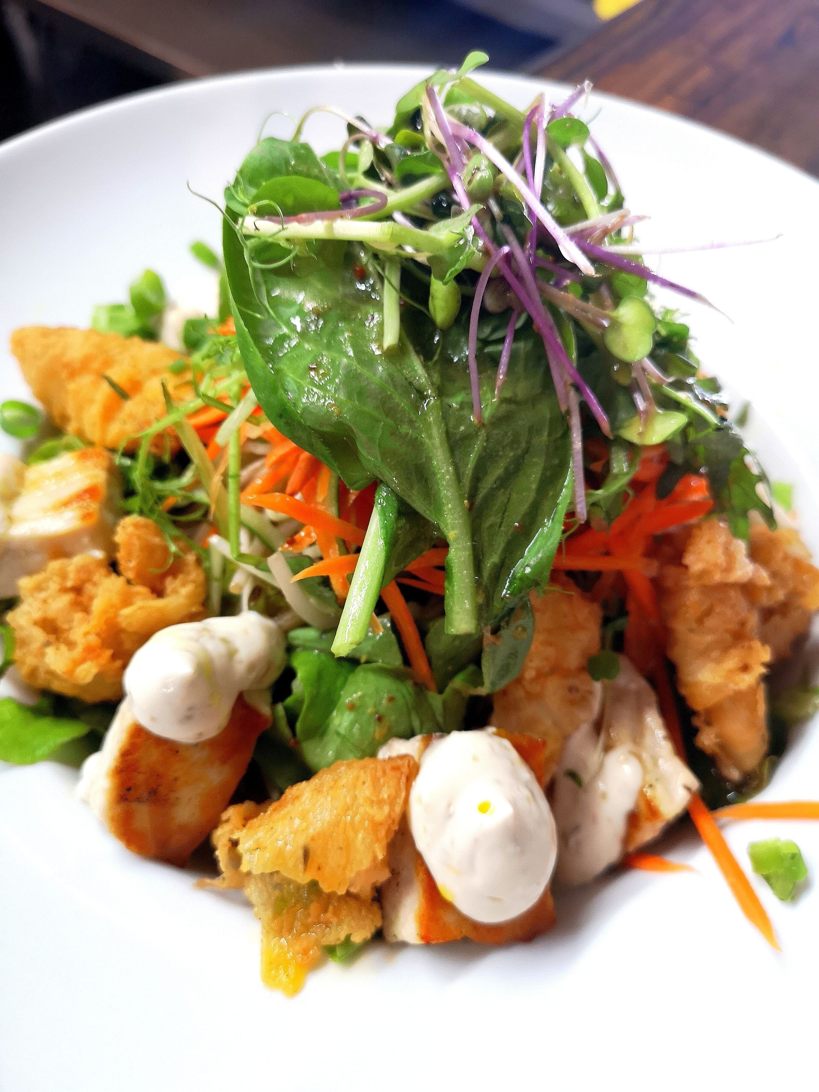 A plate of food with various ingredients including greens, carrots, and a white sauce.