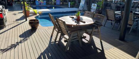 Eine Holzterrasse mit Pool, Sitzgelegenheiten im Freien und Blick auf den Ozean.