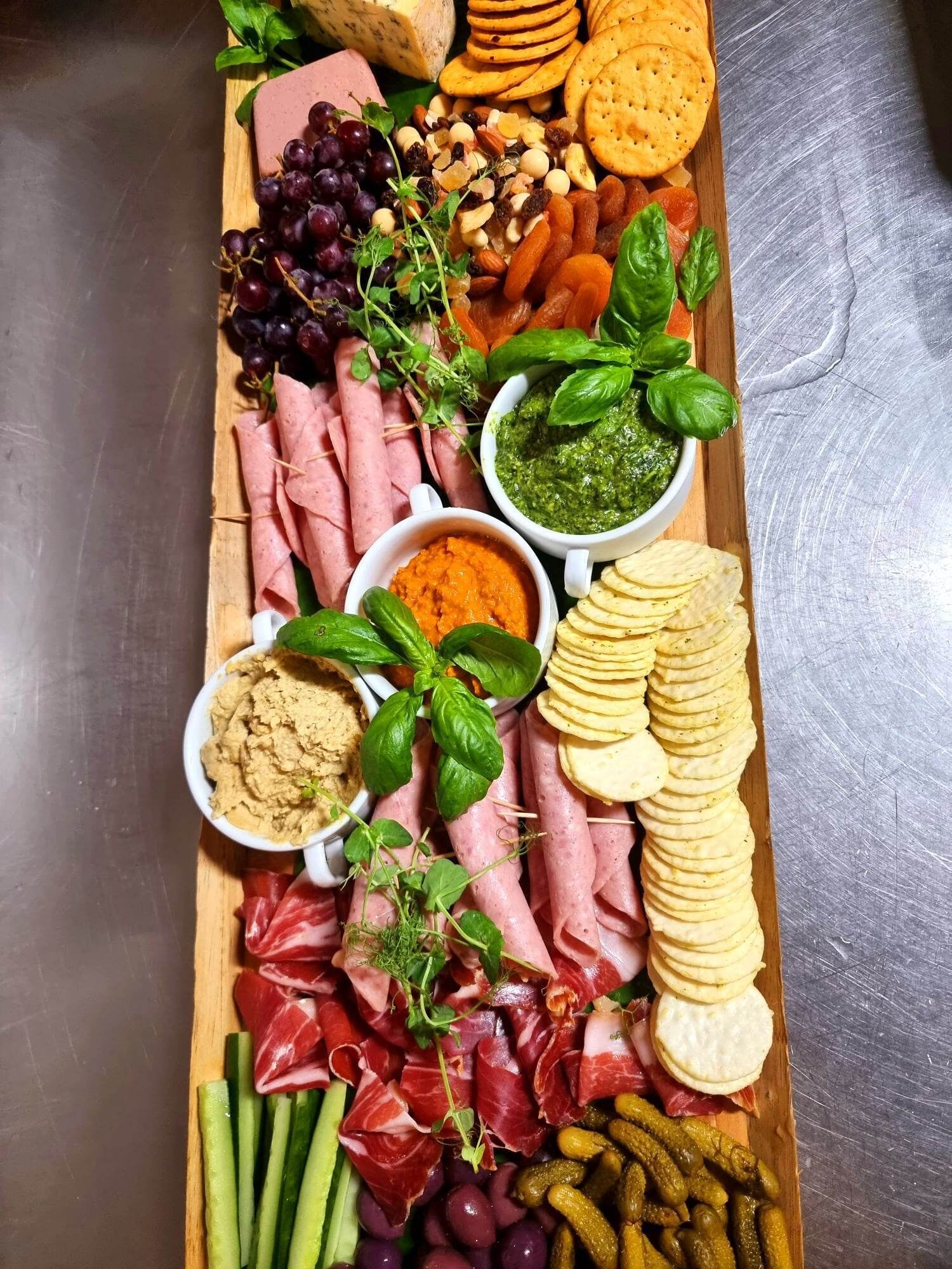 Una tabla de madera con diversos alimentos, entre ellos carnes, quesos y salsas.