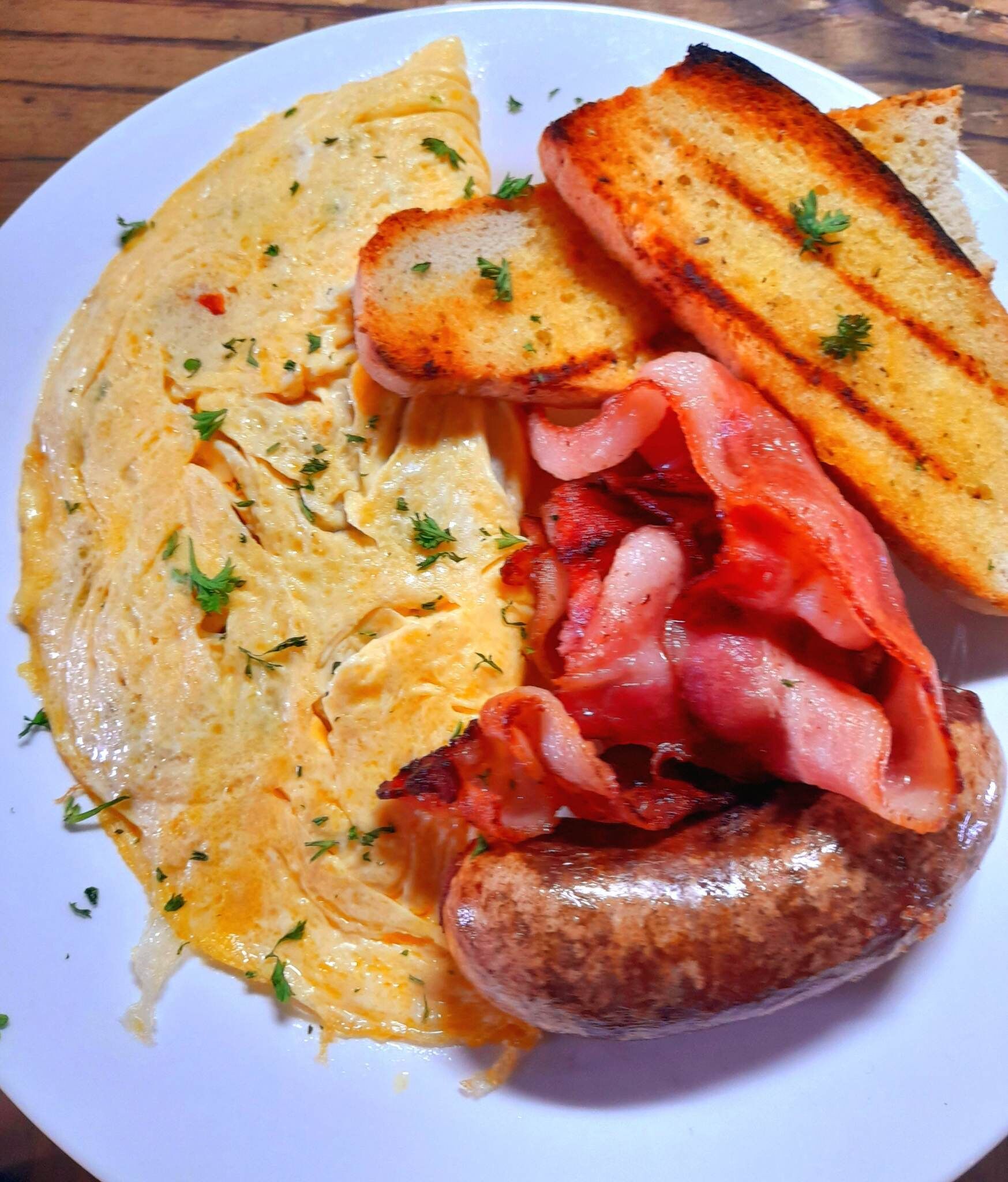 A plate with scrambled eggs, bacon, sausage, and toasted bread.