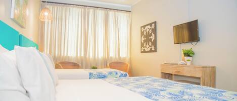 A hotel room with a bed, a desk, a chair, a TV, and a window with curtains.