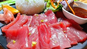 Un plato con sashimi, arroz, ensalada y salsa para mojar.