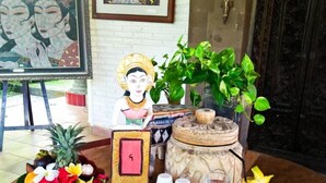 A table set with a meal, including toast, fruit, and a drink, with decorative items and a statue. - Puri Padi Hotel (Ubud)