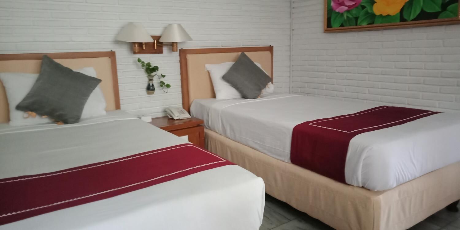 Dos camas con ropa de cama blanca y roja, una mesita de noche pequeña con lámpara y un teléfono fijo en la pared.