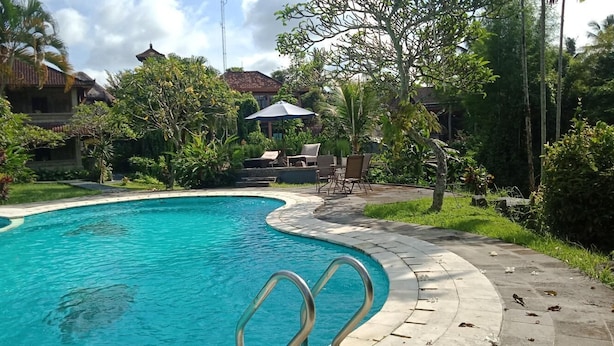 A swimming pool with a curved edge, surrounded by lush greenery and a gazebo. - Puri Padi Hotel (Ubud)