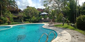 Piscina com borda curva, rodeada por vegetação exuberante e um gazebo.