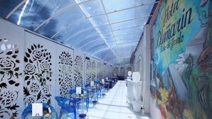 Interior moderno de hotel com mesas e cadeiras de vidro, teto curvo e um mural na parede.