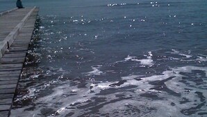 Uma praia com um calçadão de madeira e ondas quebrando na costa.