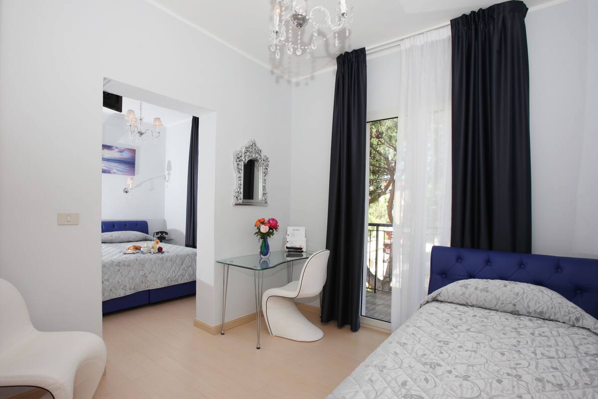 A modern hotel room with a bed, a desk, a chair, a mirror, and a view of the outdoors.