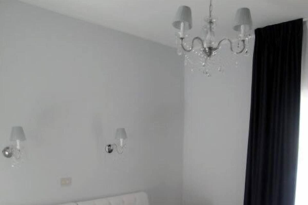 A bedroom with a large bed, a chandelier, and two wall-mounted lamps.