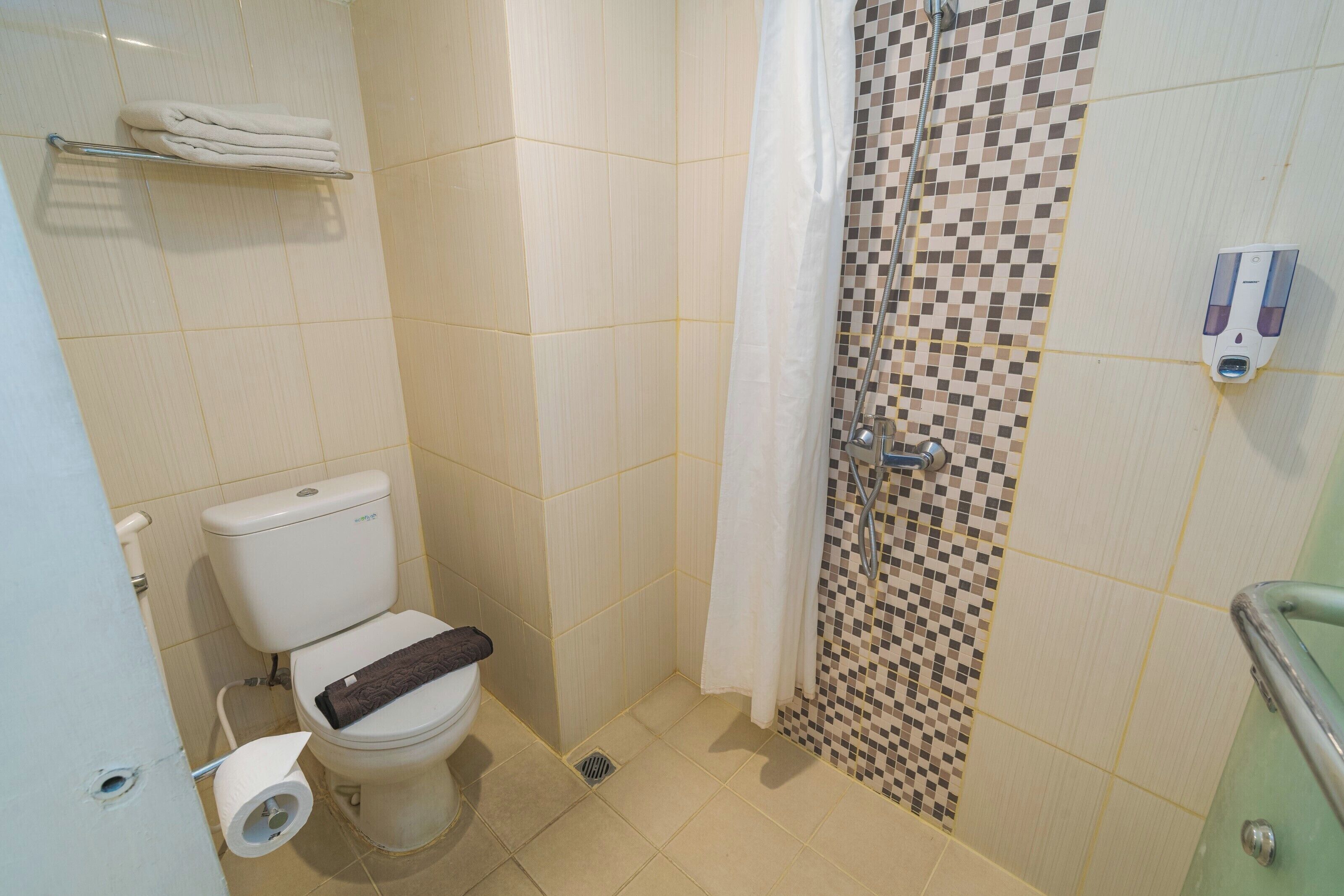 A bathroom with a toilet, a shower with a checkered tile wall, a towel rack, and a soap dispenser.