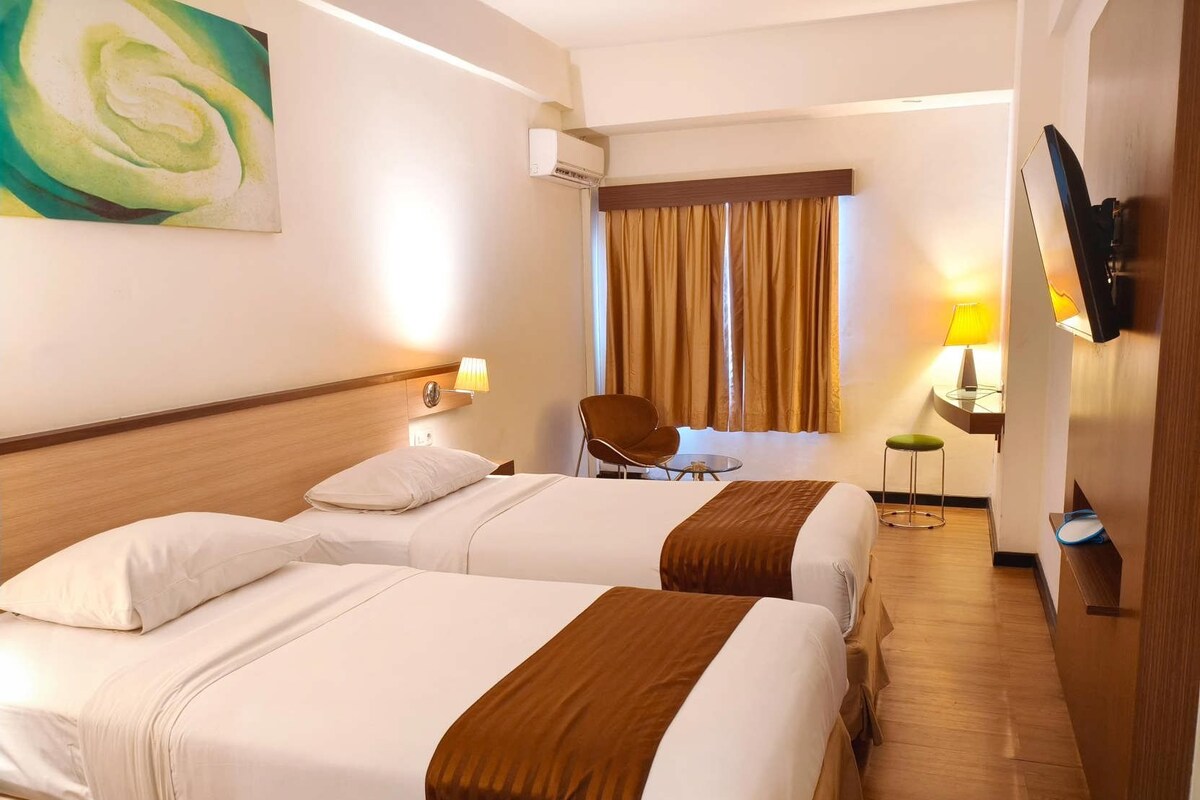 Habitación de hotel con dos camas, televisión, escritorio con lámpara y una silla.