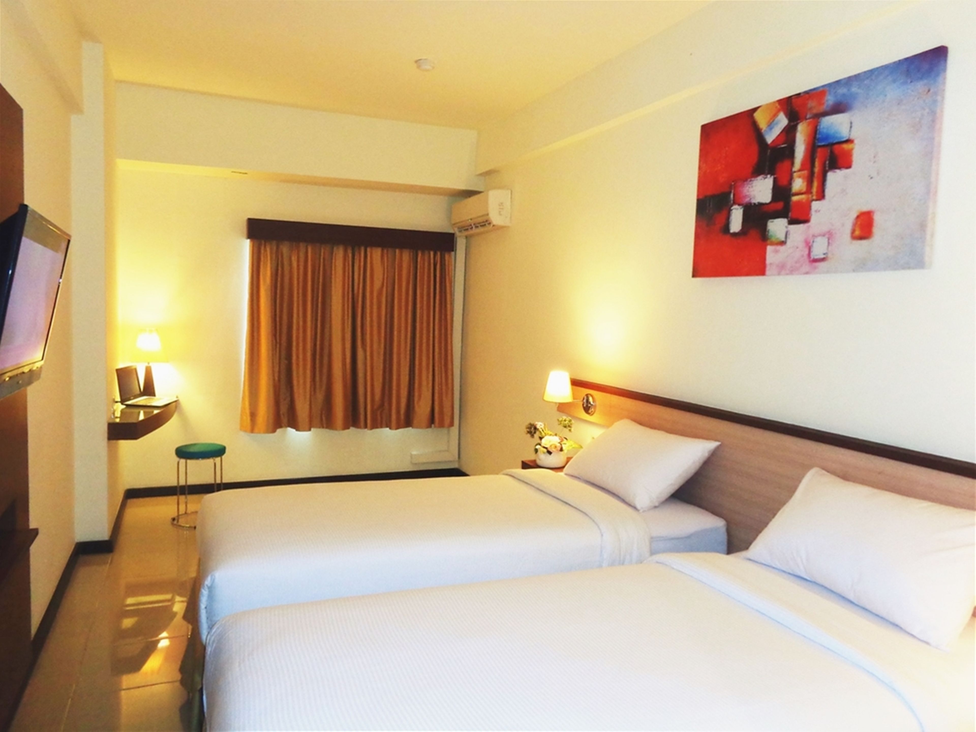 A hotel room with two beds, a flat-screen TV, a desk with a lamp, and a painting on the wall.